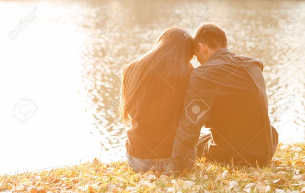 24714793-young-couple-sitting-near-lake-in-evening-heads-together-rear-view-Stock-Photo.jpg